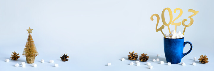 Christmas or New Year 2023 banner. Blue mug of cocoa with marshmallows and golden numbers 2023, copy space