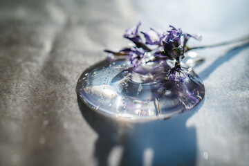 A drop of cosmetic gel with lavender flower on a beige background.