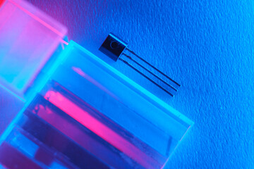 Long leg transistor on optical glass with multi-colored lighting. Neon background, soft selective focus. Disadvantage of semiconductors.