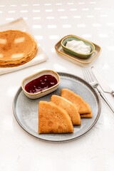 Pancakes served on a plate with sour cream and berry jam