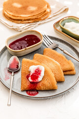 Pancakes served on a plate with sour cream and berry jam