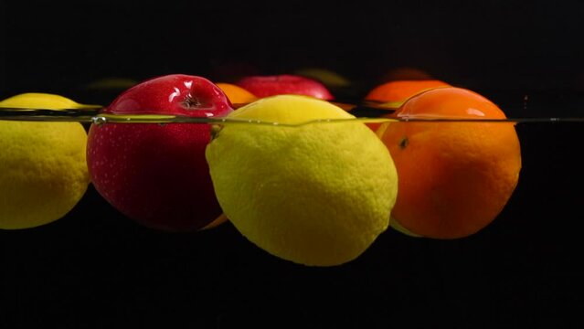 Slow motion many fruits floating on water and black background close up