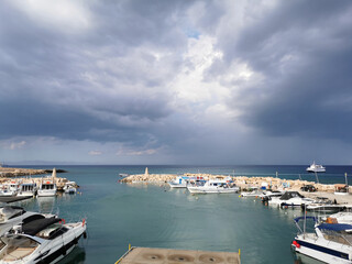 Pier, port with small ships, yachts and boats in the bay of the Mediterranean Sea against the backdrop of a dramatic sky.