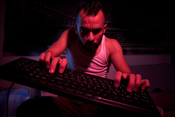 a gamer of thirty years old with a keyboard in his hands plays computer games, gets angry, feels indignation, various emotions. view from the TV side.