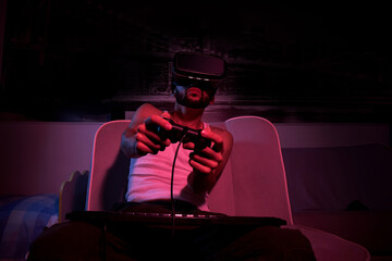 a thirty-year-old gamer in vr glasses with a keyboard and a joystick in his hands plays computer games, gets angry, feels indignation, various emotions. view from the TV side