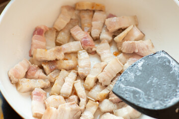 cooking spicy belly prok slice on white plate electric pan and black turner