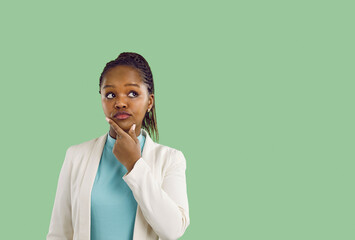 Thoughtful young African American woman isolated on green studio background look at blank copy...
