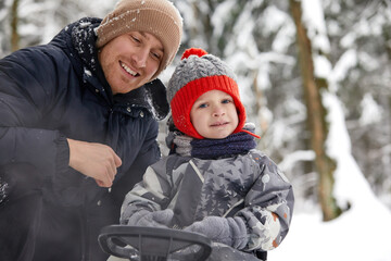 Fototapeta na wymiar Father and his son in funny hat having fun and laughing in snowy winter forest. Happy family wearing warm winter clothes enjoying wintertime in snow covered pine forest. Outdoor activities with kids.