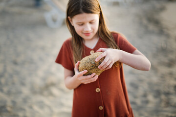 Cute long-haired European baby girl in a dress on the sea coast. Girl and stones at sunset on the...