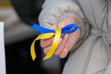 Girl with a ribbon in her hand with colors of Ukraine during a peaceful demonstration against war,...