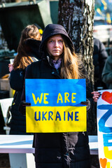 Beautiful girl or woman holding a placard We Are Ukraine during a peaceful demonstration against the war, Putin and Russia in support of Ukraine, people and flags, vertical