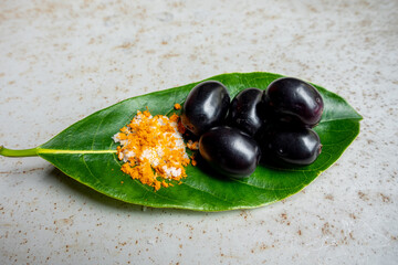 Spicy mixed salt with some black java plum fruit in the green leaves. A way to eat ripe cesium camini fruit by hand. 4k closeup video.