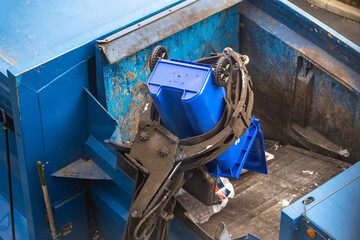 Paper and plastic are dumped into the back of a garbage truck from a trash bin.