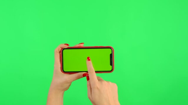 Woman holds mobile phone with workspace mock up screen in her hands on green background in horizontal position. Female hand touching, clicking, tapping, zoom in, dragging and swiping. Close up
