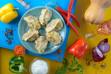 top view of delicious dumplings with sour cream and vegetables on blue and yellow background 