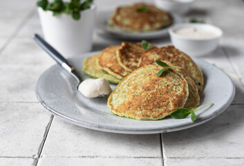Vegetable fritters served with fresh herbs and dip, tiled background. Vegetarian broccoli or spinach pancakes.