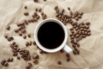 Flat lay view of black coffee cup on crumple brown paper with coffee beans