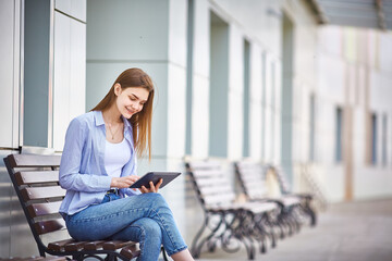 Teen girl sitting on a bench with a tablet in her hand. Copy space.