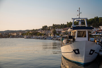 Beautiful scenic view of fishing port in Nea Skioni fishing village with popular beach and seafront restaurants. Greek marina with parked fishing boats and yachts in sunset.