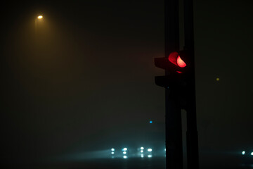 Closeup view of semaphore, red light and foggy night atmosphere. Car lights and traffic in...