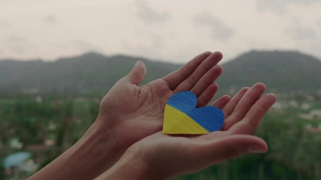 Female hands hold in hand Ukrainian flag symbol in the form of heart. Save Ukraine. Pray for our country