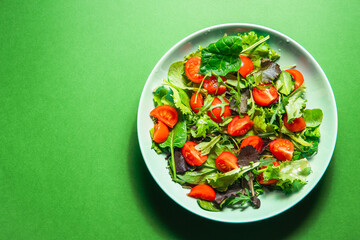 Healthy fresh salad of vegetable, tomato, spinach, arugula in a green plate. Food background for menu, recipe. Top view. salat with tomatoes cherry and green leafs. 