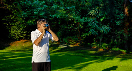 The golfer accurately measures the distance to the flag in a golf course with the laser rangefinder. In the background the forest.