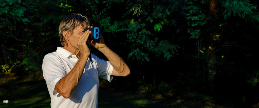 The Golfer Accurately Measures The Distance To The Flag In A Golf Course With The Laser Rangefinder. In The Background The Forest.