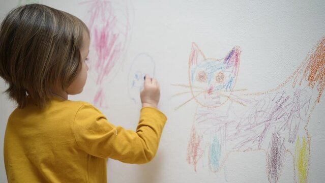 Cute adorable small kid girl artist drawing coloring picture with chalk, crayon on white wall, focused smart preschool child enjoying creative art hobby activity at home, children development concept