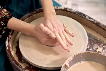 Dirty hands of a ceramist make a cup of clay on a potter's wheel.
