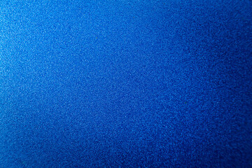Blue abstract surface with grainy texture. A blue matte background with focus in the middle and blurring at the top and bottom.