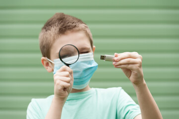 hand holding a flash drive and a boy examining it through the magnifying glass in the blurred...