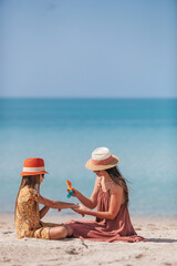 Young mother applying sun cream to daughter nose on the beach. Sun protection