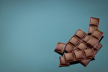 Broken dark chocolate bar on a blue background, space for text.