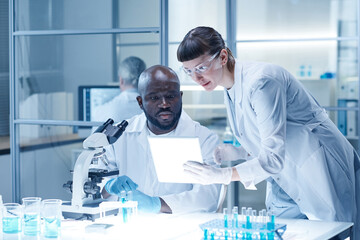 Woman showing the results of analysis on tablet pc to her colleague while he sitting at table with...