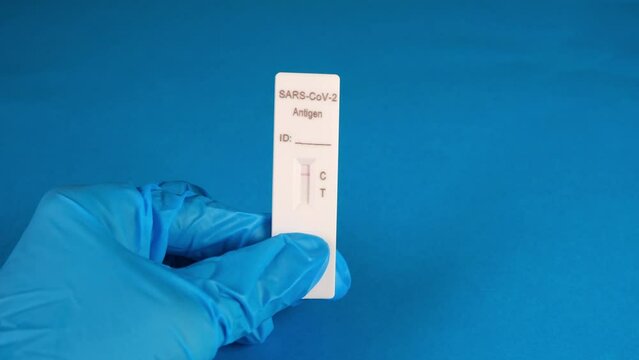 hand in a protective medical glove holds a Negative SARS-CoV-2 Rapid Antigen Test on a blue background
