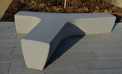 in the square stands a gray, white bench made of artificial stone. T or Y-shaped concrete casting. Perennial flower beds in winter covered with frost in the morning sun.