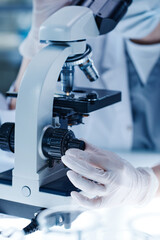 Close-up of scientist adjusting the lenses of a microscope during medical exam in laboratory