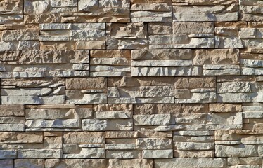 Stone wall cladding made of stacked irregular and horizontal rock strips,  under sunlight . Colors are white and light brown.