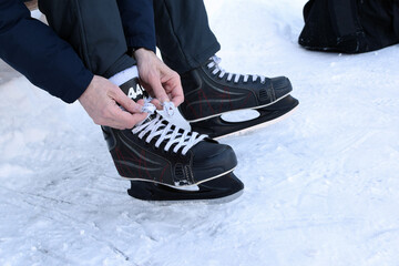 Man puts on hockey skates and ties his shoelaces on an outdoor ice rink.