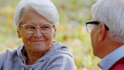 Elderly grey-haired grandparents smiling at each other and talking while spending time outdoors. High quality photo