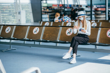 Young student college girl sitting at airport terminal wear medical mask feeling happy with safety travel bubble plan after covid pandemic and waiting for flight in fit to fly in concept.