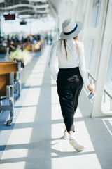 Obraz premium Young woman near window in an airport lounge waiting for flight aircraft. woman at the airport stands with tickets, overall plan.
