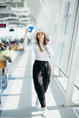 Cheerful businesswoman waiting for her flight at airport. Young woman at the airport. Woman is waiting her flight in waiting hall in airport. Happy traveler woman is waiting for a flight.