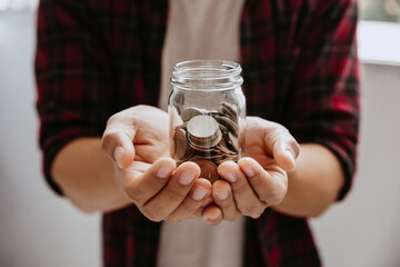 Young man hold coins in jar glass.