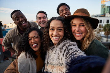 Multi-cultural group of friends taking a selfie at a rooftop party. Smiling and posing at camera in the city.