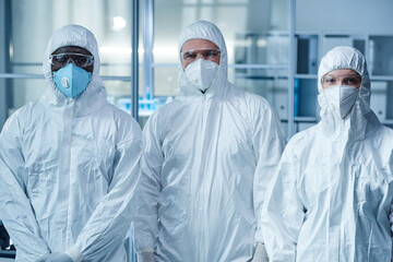 Portrait of group of doctors in protective wear and masks looking at camera while working in team in laboratory