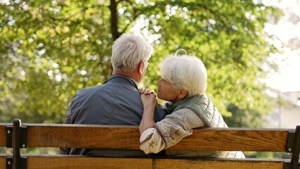 Elderly caucasian woman sitting together with her husband leans towards her grey-haired spouse and hugs him. Happy retirement concept. High quality photo