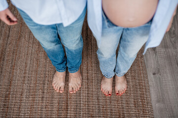 The legs of a man and a woman in blue pants and the belly of a pregnant woman