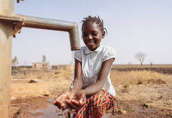 Gorgeous young black African village girl smiling happily at the clean water flowing out of the...